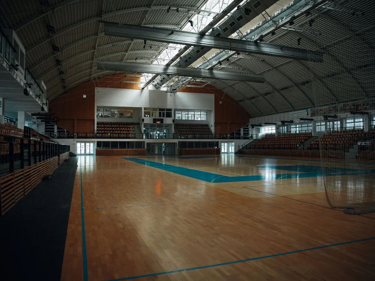 Imagen de referencia: pabellón deportivo cubierto con cancha de madera y gradas (fotografía de archivo, no es una obra de Constructora G2)